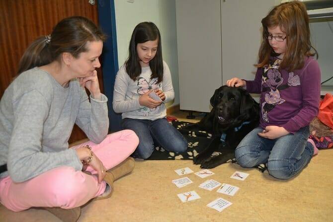 Tiergestützte Arbeit Ausbildung - Frau und zwei Kinder und Hund spielen Karten