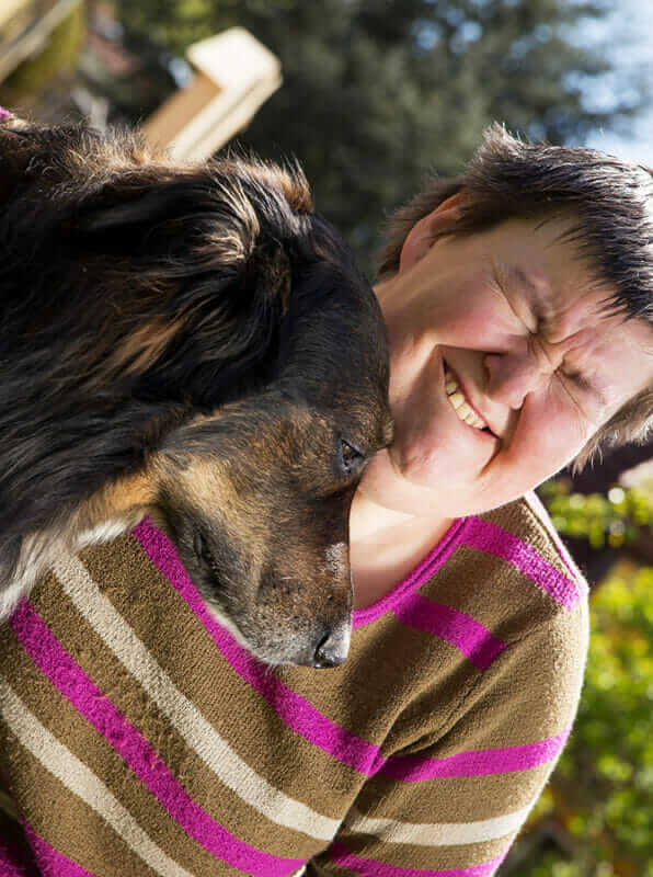 Assistenzhundetrainer Ausbildung - behinderte Frau umarmt Hund im Freien