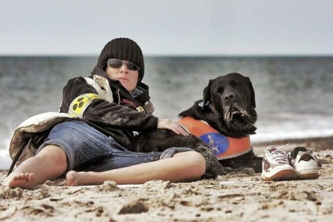 Assistenzhundetrainer Ausbildung - blinder junger Mann mit Assistenzhund am Strand