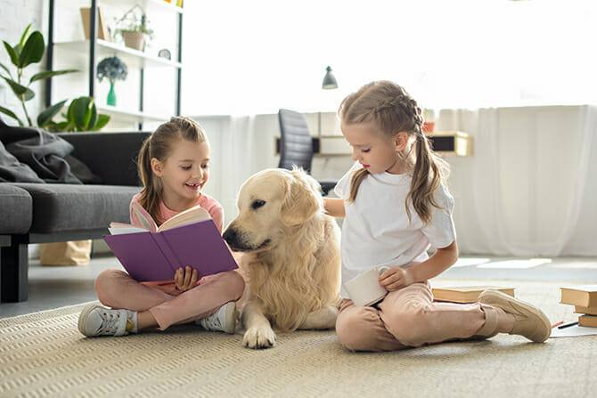 Therapiebegleithunde Trainer Ausbildung - junge Schwestern sitzen mit Buch und Golden Retriever auf dem Boden im Wohnzimmer