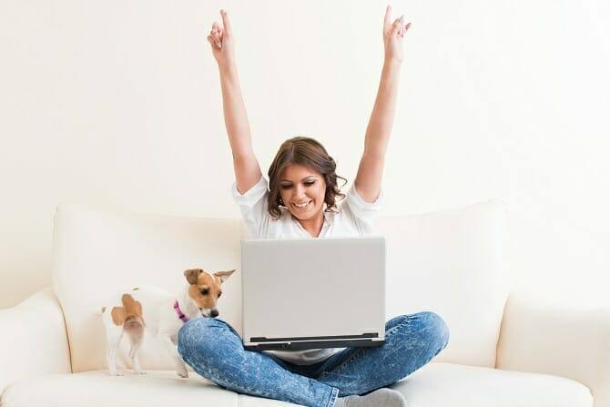 ATN Akademie - Junge Frau in Siegerpose vor Laptop mit Hund auf Couch
